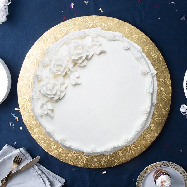 A white cake with white frosting and flowers on a gold Enjay round cake drum on a table.