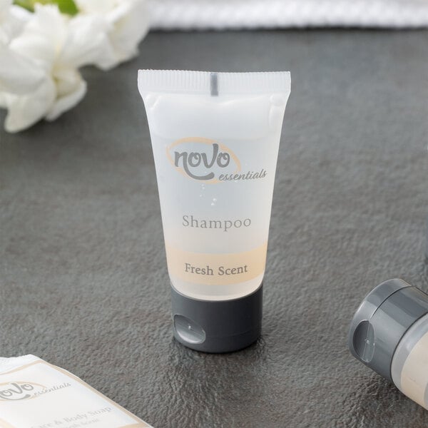 A small white bottle of Novo Essentials Hotel Shampoo on a table.