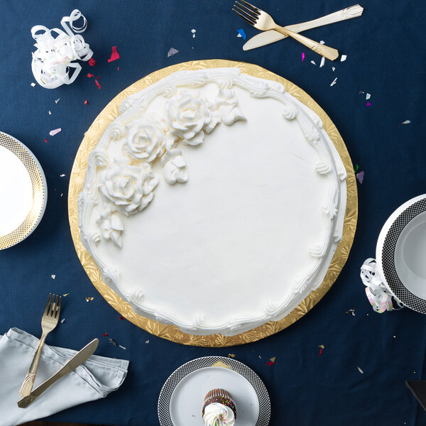 A white cake with white frosting and flowers on a gold round cake drum.