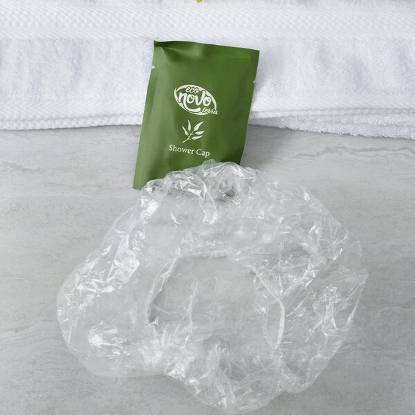 A green plastic bag with a white Noble Eco Novo Terra shower cap inside on a white towel.