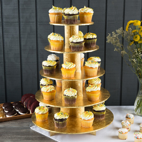 A Enjay gold tiered cupcake stand holding cupcakes with yellow, white, and frosted decorations.