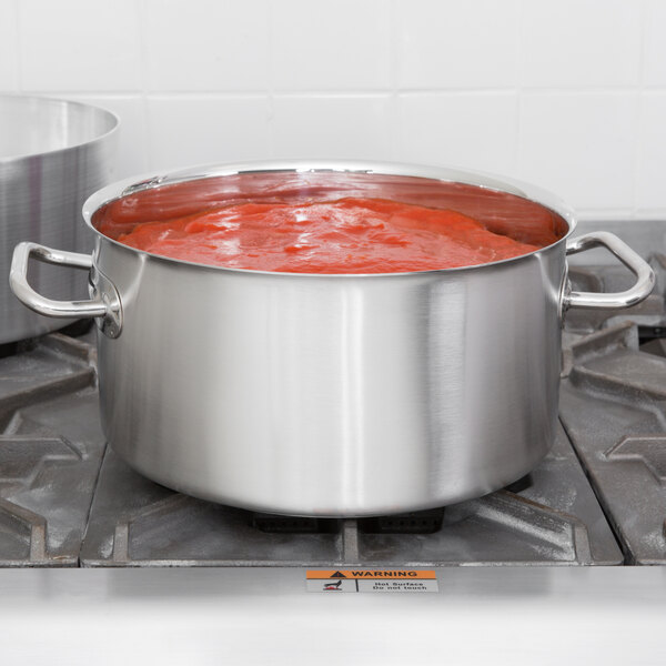 A silver Vollrath sauce pot filled with red sauce on a stove.