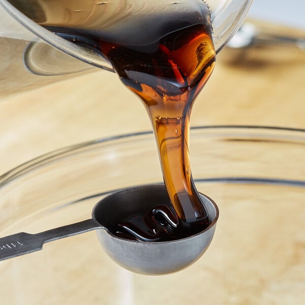 A spoon pouring dark corn syrup into a glass cup.