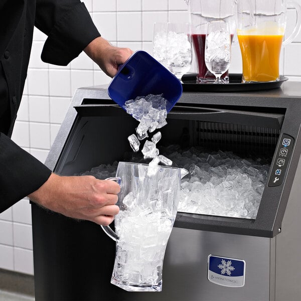 A person pouring ice from a blue bucket into a Manitowoc undercounter ice machine.