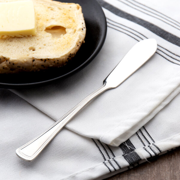A Oneida Needlepoint stainless steel butter knife on a plate with a piece of bread and butter.