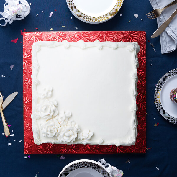 A white square cake on a red Enjay cake drum with white flowers on top.