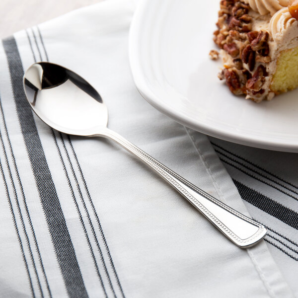 A Oneida Needlepoint stainless steel oval bowl spoon on a plate with cake.