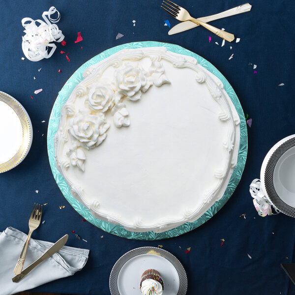 A white cake with white frosting on a blue Enjay round cake drum on a blue table with silverware.