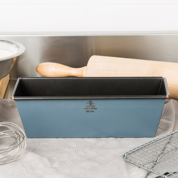 A Matfer Bourgeat steel non-stick flared bread loaf pan on a counter with a wire grid and a rolling pin.