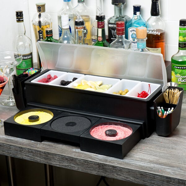 A Tablecraft 5-compartment condiment bar on a counter in a cocktail bar with glass rimming trays on it.