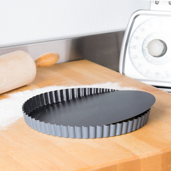 A Matfer Bourgeat fluted non-stick tart pan with a removable bottom on a wooden surface.