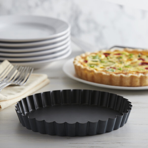 A black round Matfer Bourgeat fluted pan with a slice of quiche on a table