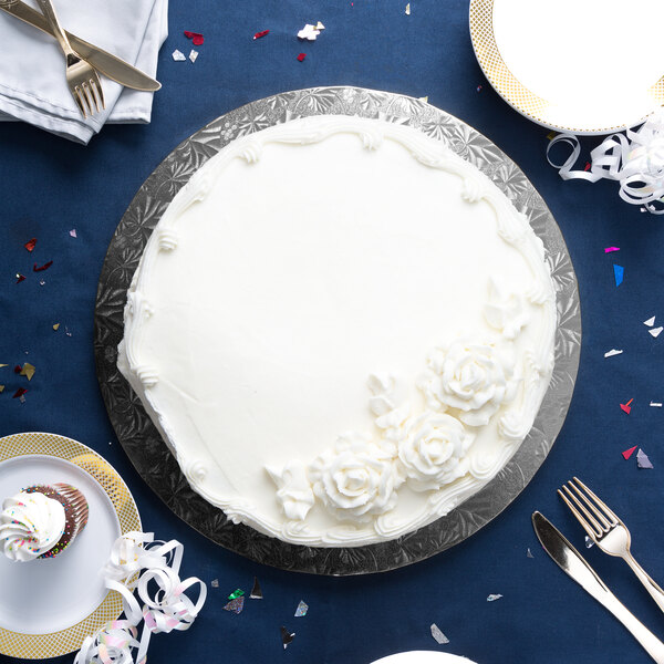 A white cake with frosting on a black Enjay round cake drum on a blue table with silverware.