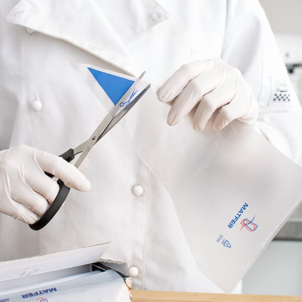A person in a white coat cutting a Matfer Bourgeat disposable pastry bag with scissors.