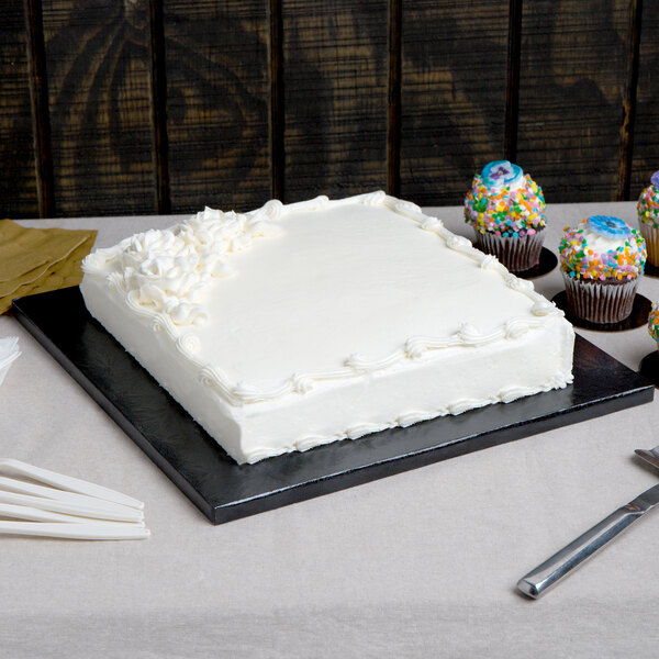 A white frosted cake on a black Enjay square cake board.