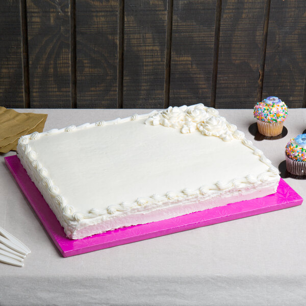 A white cake on a table with a pink Enjay 1/2 sheet cake board underneath.