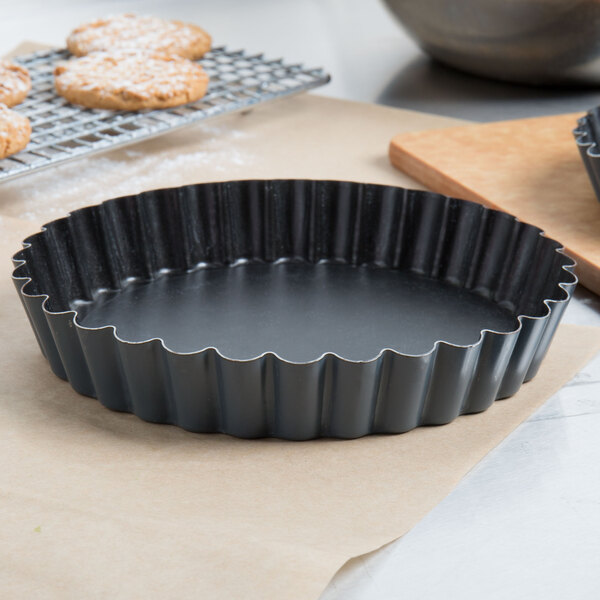 A black Matfer Bourgeat fluted cake / tart pan with scalloped edges on a table.