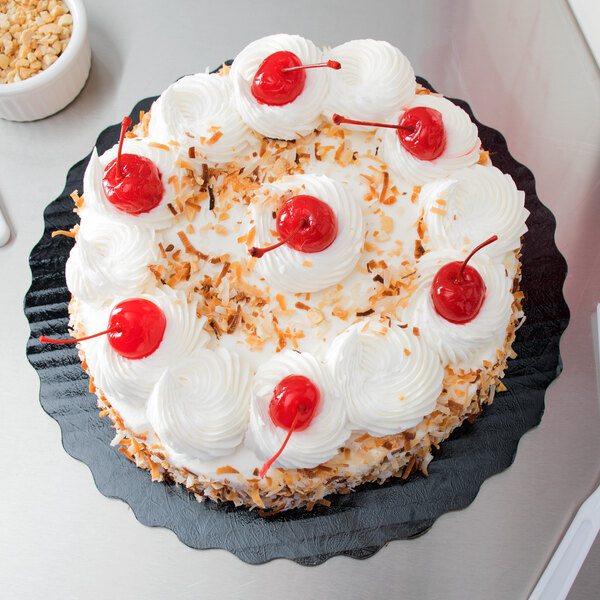 A cake with whipped cream and cherries on a black Enjay laminated cake circle.