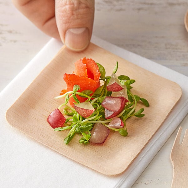 A hand holding a Bamboo by EcoChoice square plate with vegetables on it.