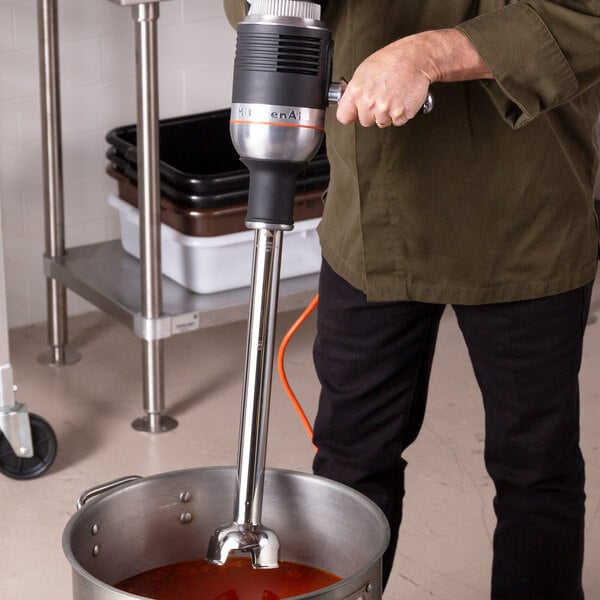 A man using a KitchenAid 400 Series immersion blender to mix liquid in a professional kitchen.