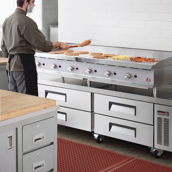 A man cooking food on a large stainless steel countertop griddle.
