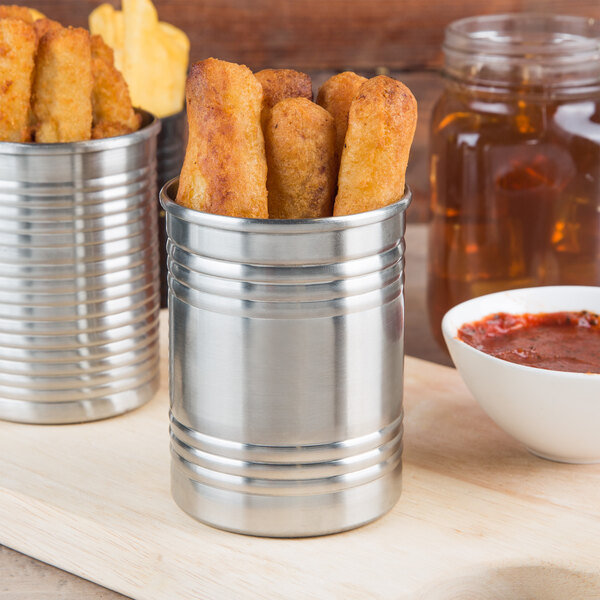 French fries in a metal can with red sauce on a cutting board.