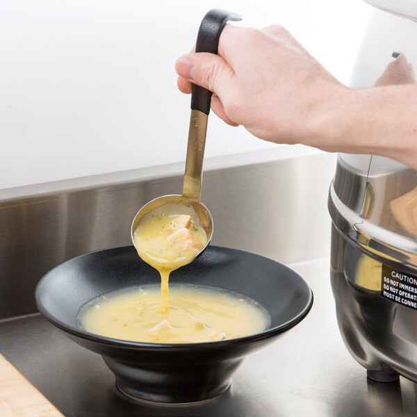 A hand holding a Vollrath ladle with a black handle pouring soup into a bowl.