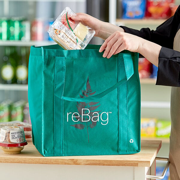 A person holding a ReBag reusable green grocery bag with food inside.