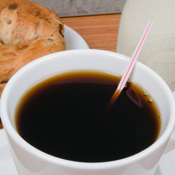 A white cup of coffee with a red and white Choice coffee stirrer on the counter next to a bagel.