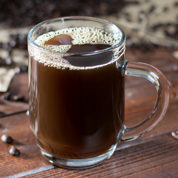 A Libbey glass coffee mug filled with brown liquid and coffee beans.