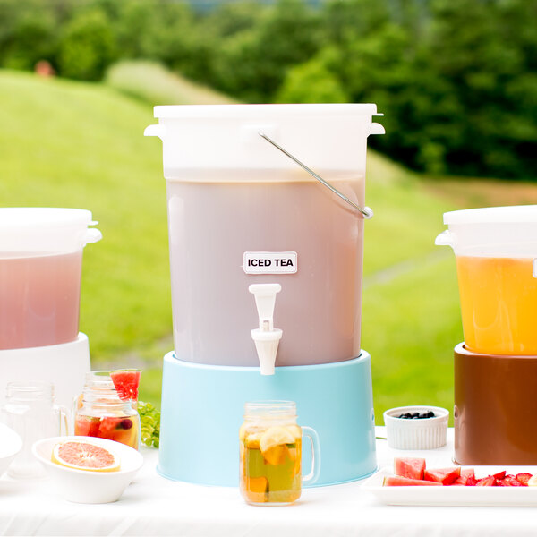 A Choice white beverage dispenser with a blue base on a table with containers of iced tea.