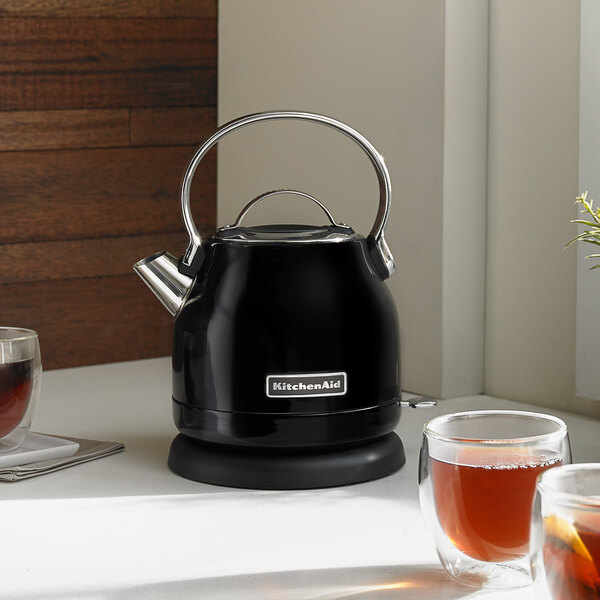 A black KitchenAid electric kettle on a table with tea cups.