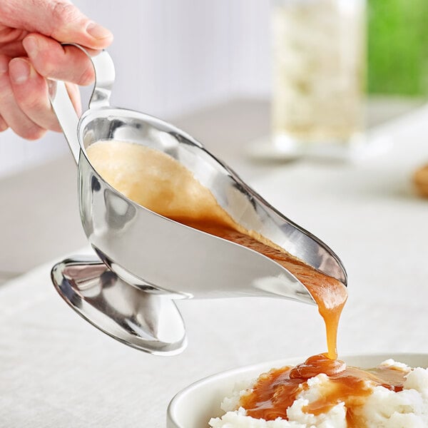 A person pouring brown liquid into an American Metalcraft stainless steel gravy boat.