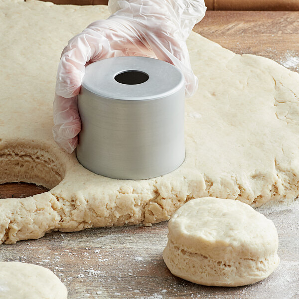 A person's hand using an American Metalcraft round metal biscuit cutter on dough.