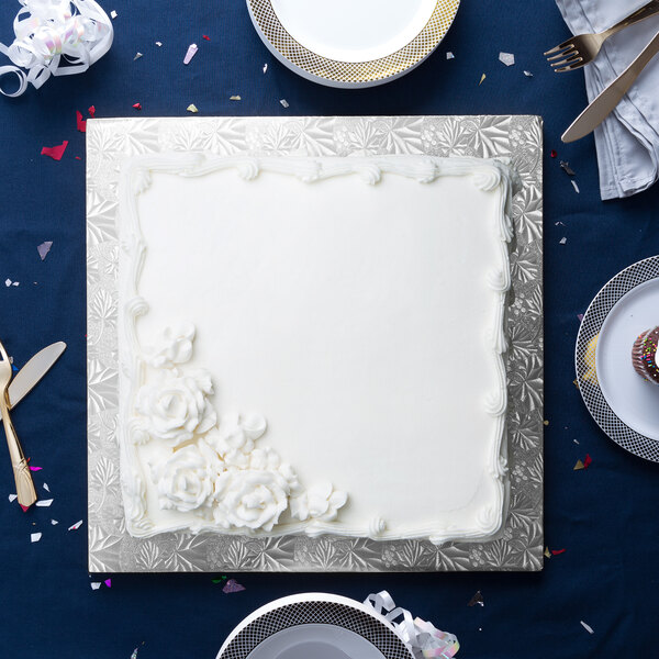 A white square cake on a silver square cake drum with white frosting.