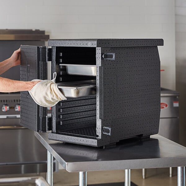 A woman using a Cambro Cam GoBox food pan carrier to load a metal tray of food in a professional kitchen.