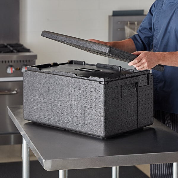 A person opening a black Cambro Cam GoBox on a black surface.