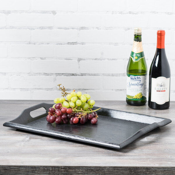 A black GET room service tray on a table with a plate of grapes and bottles of wine.