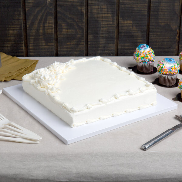 A white cake on a white Enjay square cake drum on a table.