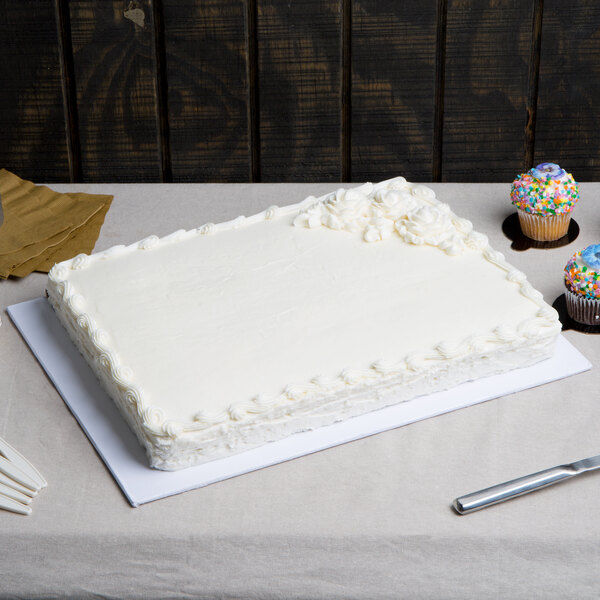 A white Enjay 1/2 sheet cake board under a white cake with frosting on a table.
