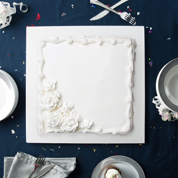 A white square cake with frosting flowers on a white Enjay cake board.