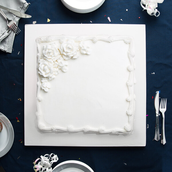 A white square cake with white frosting and flowers on a table with a white Enjay 18" square cake drum.