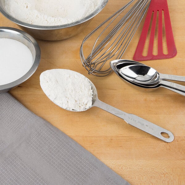 A stainless steel Vollrath measuring scoop with flour on a table.