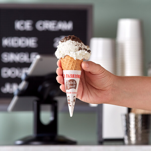 A hand holding a Dutch Treat sugar cone filled with ice cream.