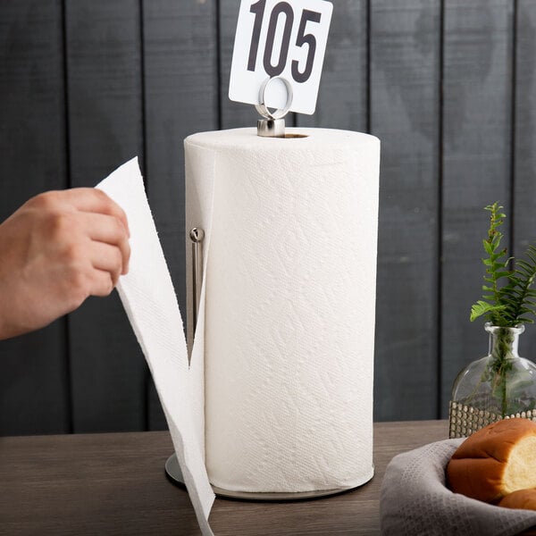 A hand holding a paper towel roll with a number card inserted into a stainless steel holder.