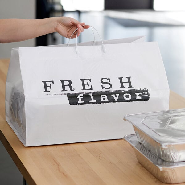 A hand holding a white rigid plastic shopper bag with black text reading "Fresh Flavor" next to foil containers.