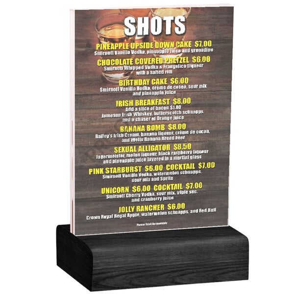 A Menu Solutions clear acrylic table tent with a black wood base holding a menu on a wood surface.