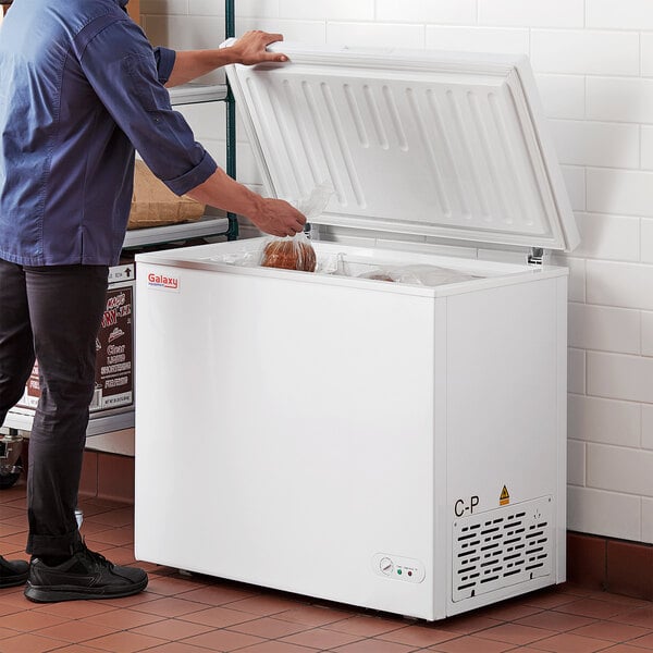 A man opening a Galaxy commercial chest freezer in a professional kitchen.