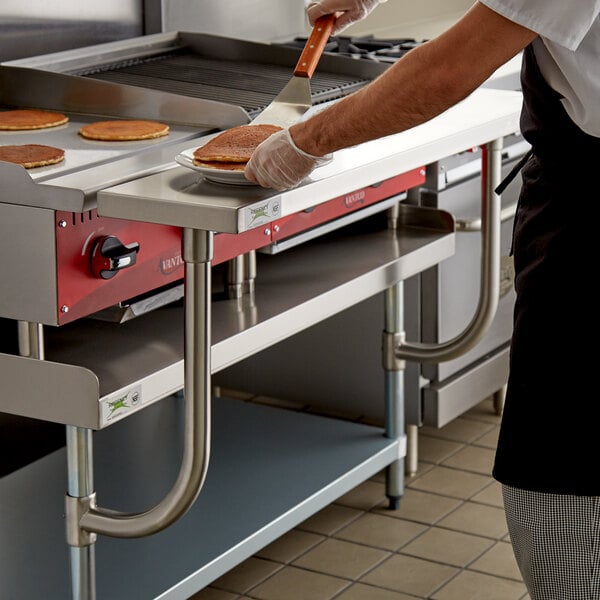 A man using a Regency stainless steel work surface in a commercial kitchen to cook pancakes.