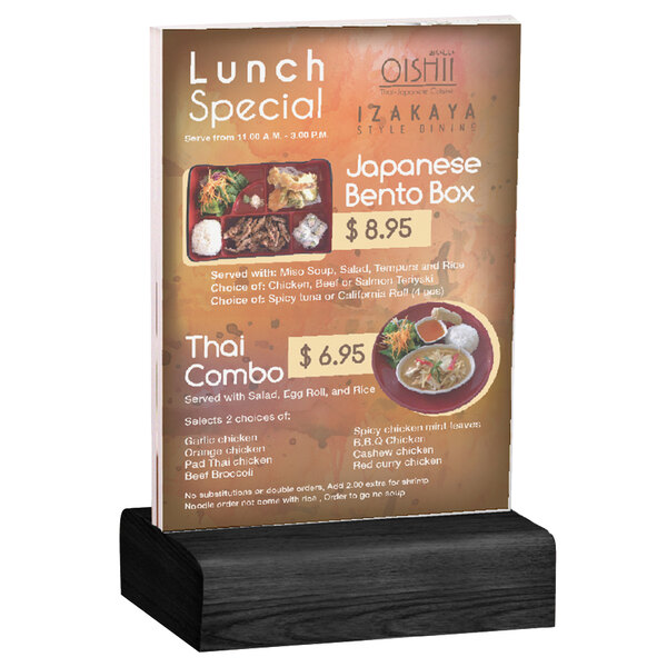 A Menu Solutions clear acrylic table tent with a solid black wood base on a wooden table.